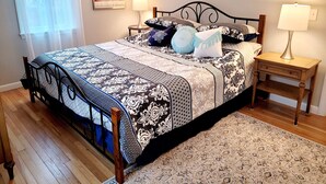 A bedroom with a bed, two bedside tables, a lamp on each table, a patterned bedspread, a rug, and a painting on the wall. - 2 bedroom ranch 1 bath situated in West Yarmouth (Yarmouth)