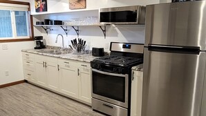 A modern kitchen with white cabinets, stainless steel appliances, and a wooden floor.