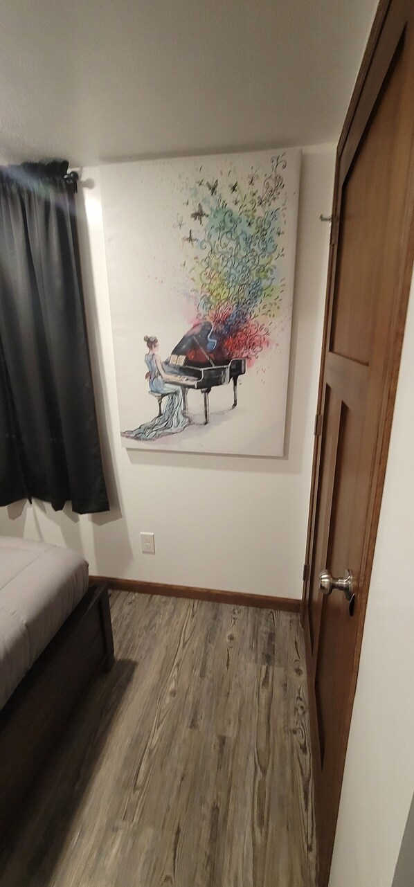 Una habitación con cama, puerta y pared con un cuadro de una mujer tocando el piano.