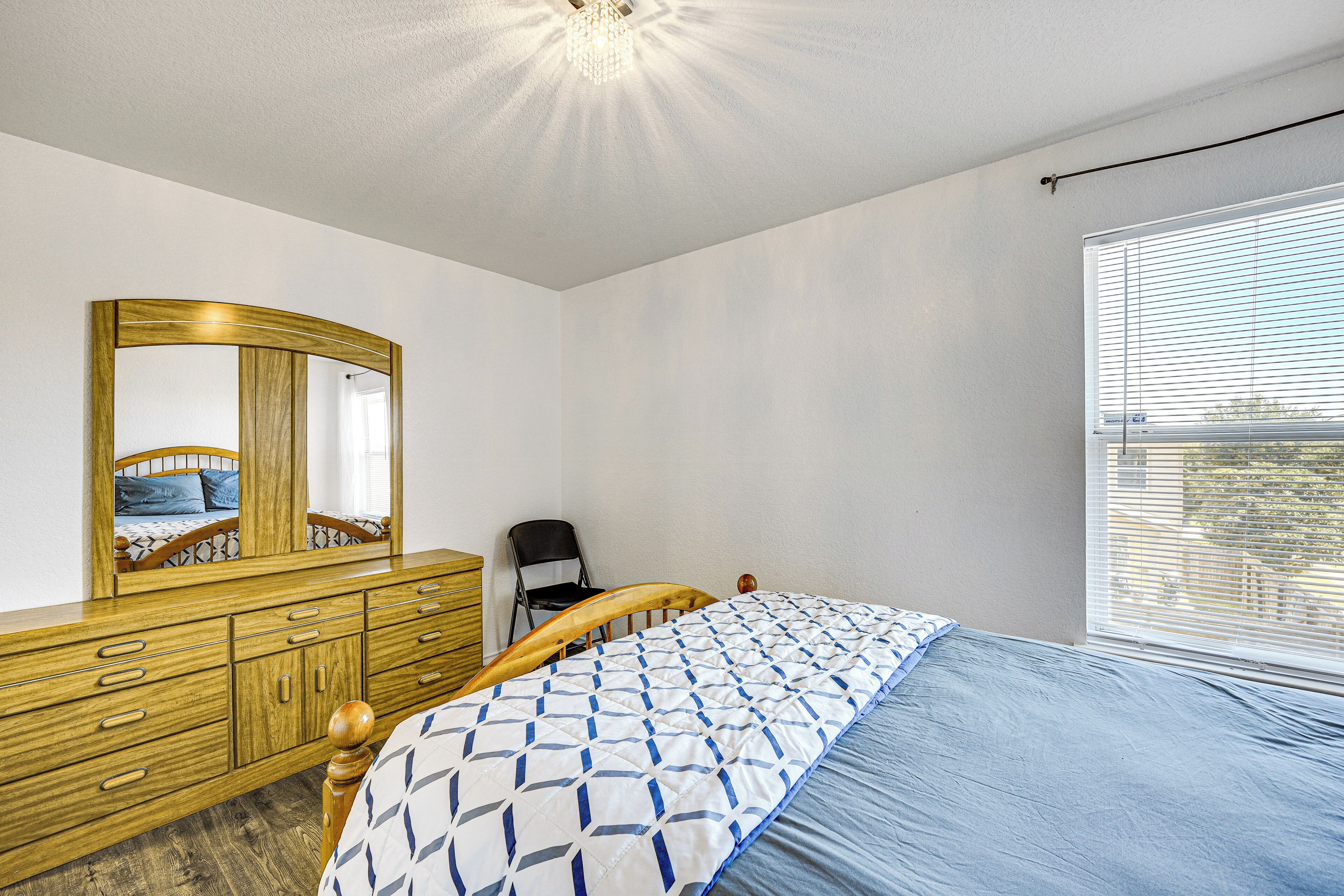 Un dormitorio con cama de madera, cómoda con cajones, espejo y ventana con persianas.