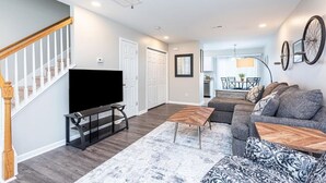 A modern living room with a flat-screen TV, a sectional sofa, and a wooden coffee table. - Beautifully Furnished, Raleigh Townhome Retreat (Raleigh)