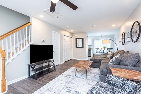 A modern living room with a flat-screen TV, a sectional sofa, and a wooden coffee table. - Beautifully Furnished, Raleigh Townhome Retreat (Raleigh)