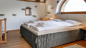 Un dormitorio con techo de madera, paredes de piedra, una cama con sábanas blancas y un ventanal pequeño.