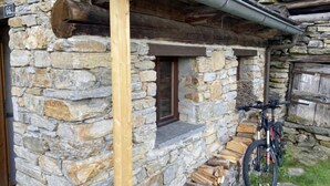 Un edificio de piedra con una escalera de madera que lleva a una puerta, una bicicleta estacionada afuera y un muro de piedra con una ventana.