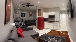 Ein kompakter Wohnraum mit Sofa, Esstisch, Küchenzeile und Deckenventilator.