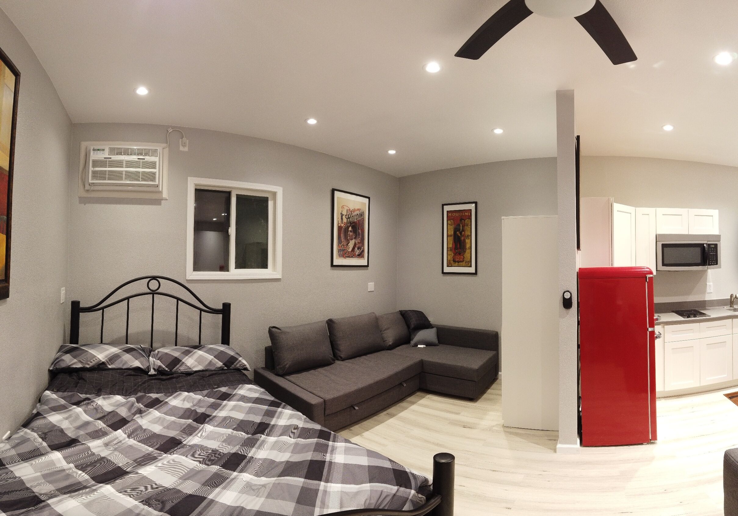 Ett kompakt bostadsutrymme med en säng, en soffa, ett litet kök och ett rött kylskåp.
