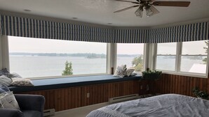 Ein Schlafzimmer mit einem großen Bett, einer Sitzgelegenheit am Fenster mit Seeblick und einem Deckenventilator.