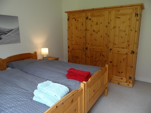 Een slaapkamer met een bed, een nachtkastje met lamp en een houten garderobe.
