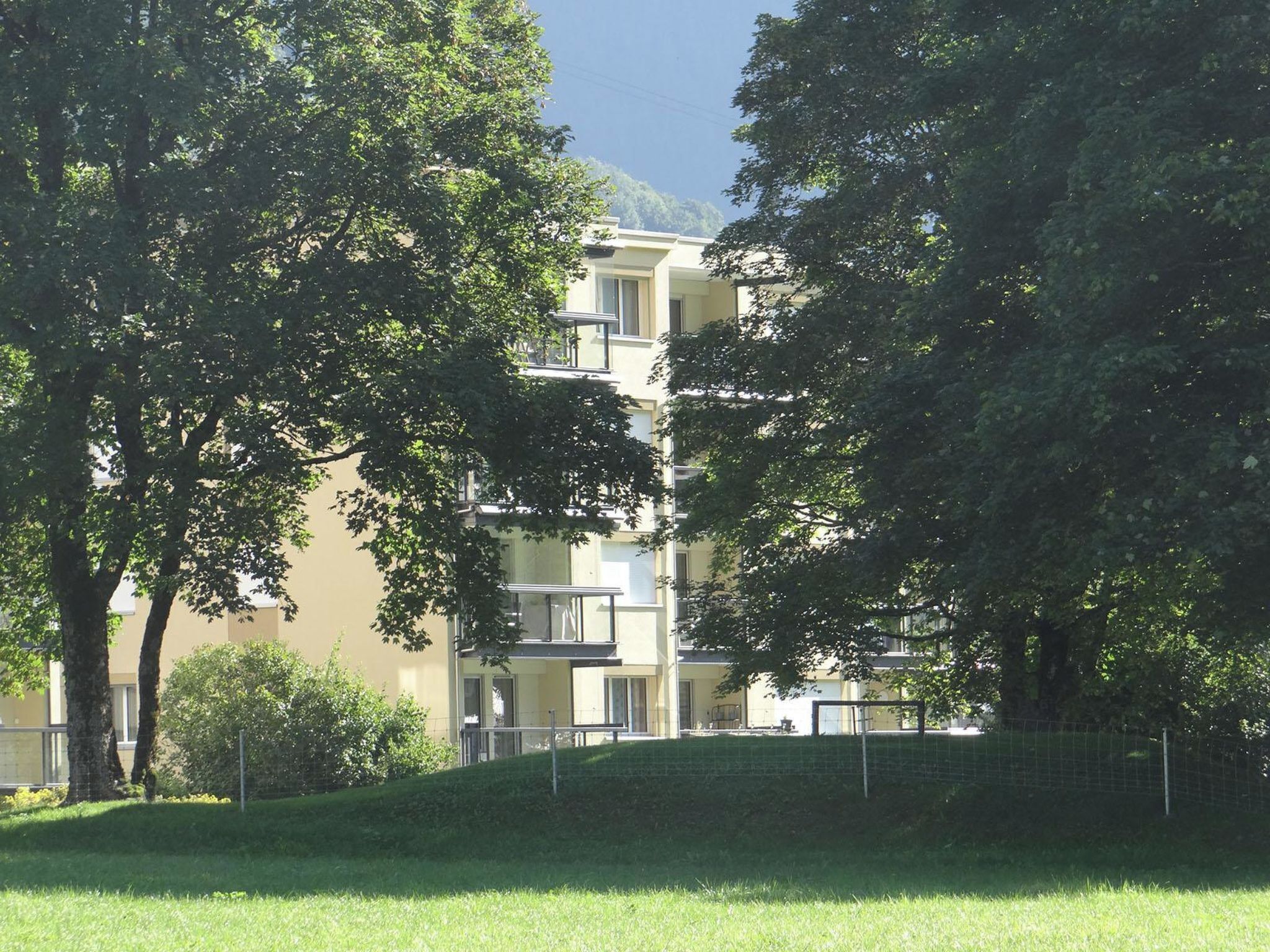 Un immeuble résidentiel à plusieurs étages, doté de balcons, entouré d’arbres et d’une zone herbeuse.