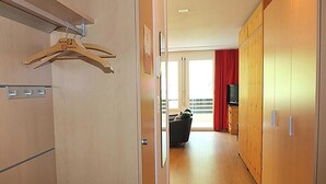 A hotel corridor with wooden flooring, a coat rack, a television on a cabinet, and a balcony with red curtains. - Erlenrain Wohnung 722E Appartement/Fewo 2-Bettwohnung by Interhome (Engelberg)