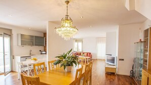 Ampla sala de estar com mesa de jantar de madeira, um lustre e sofá vermelho.