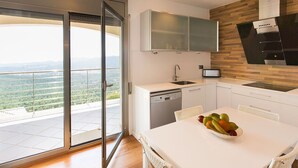 Cozinha moderna com uma janela grande, área de jantar com um cesto de frutas e vista para o horizonte da cidade.