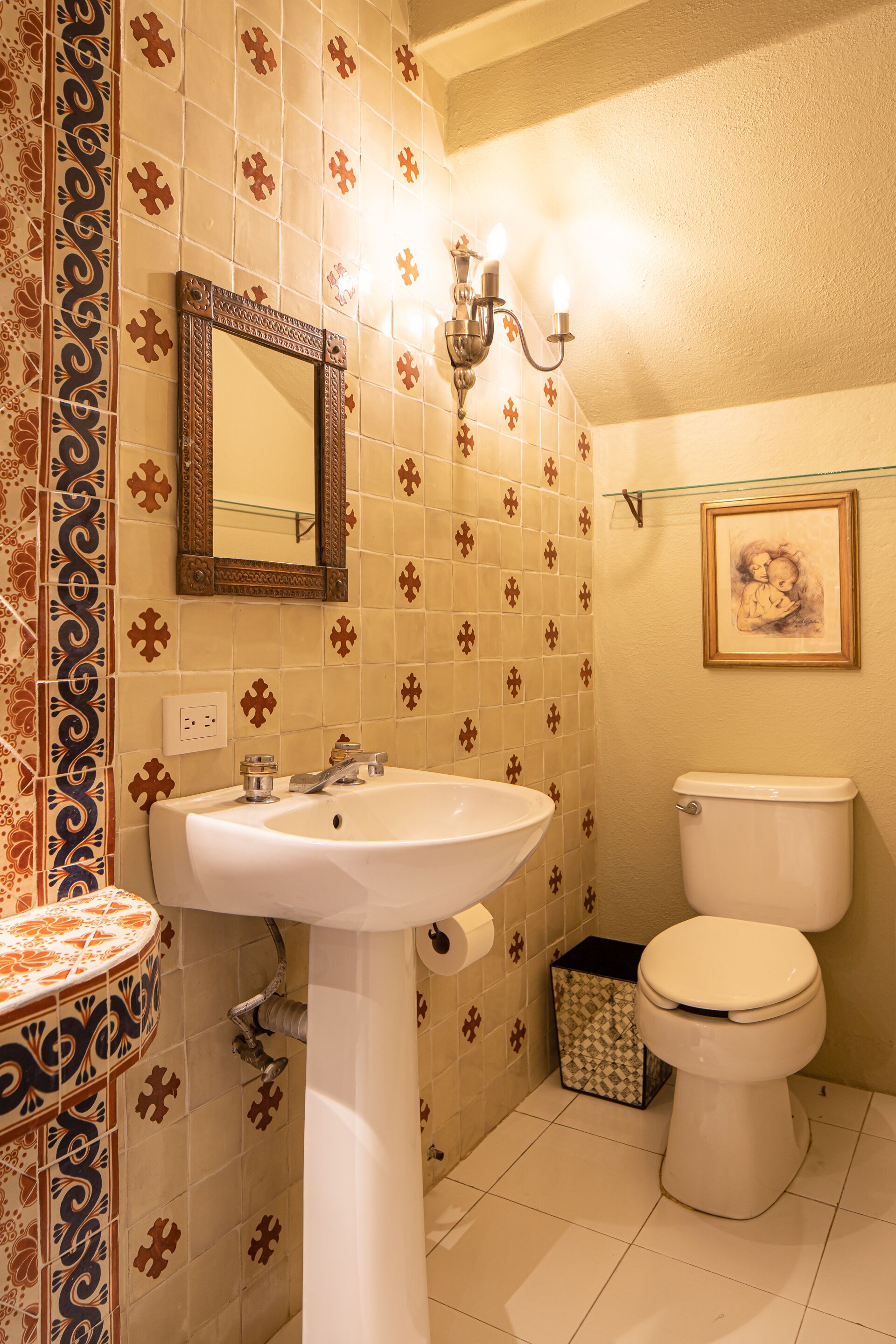 A bathroom with a white sink, a mirror, a toilet, and patterned tiles.
