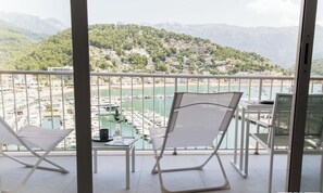 A balcony with two white chairs, a table, and a view of a marina with boats and a hillside town. - YourHouse Es Niu, apartamento in Puerto de Sóller, between the sea and the montains (Sóller)