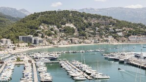 Un puerto deportivo con numerosas embarcaciones amarradas, una playa y edificios en una colina.