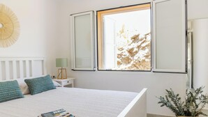 Un dormitorio con cama, almohadas, una mesita de noche, una lámpara y una ventana con vistas a un paisaje rocoso.