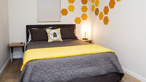 Ett sovrum med en säng, ett sängbord, ett litet bord vid sängen, en lampa och en vägg med hexagonformade mönster.