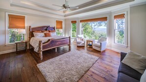 A bedroom with a wooden bed, a ceiling fan, and large windows with blinds. - Big Canoe Home with Mountain Views, Game Room, Fire Pit, Sleeps 14 (Big Canoe)