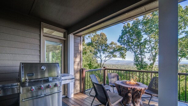 A covered deck with a stainless steel grill, two wicker chairs, and a fire pit. - Big Canoe Home with Mountain Views, Game Room, Fire Pit, Sleeps 14 (Big Canoe)