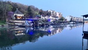 Un lago tranquilo con barcos amarrados, un edificio de fachada de vidrio y un paisaje montañoso cubierto de bosque al fondo.