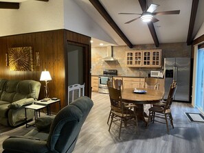 Una sala de estar moderna con un sofá, una mesa de comedor con sillas, un ventilador de techo y una cocina con armarios y electrodomésticos.