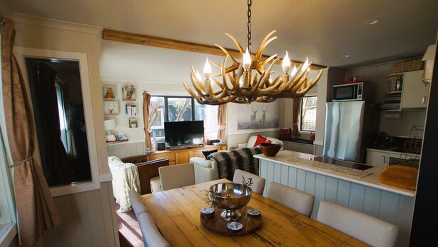 A dining area with a wooden table, white chairs, and a large chandelier. - Mountain Retreat Suitable for 2 Families, Sleeps 8 (Mount Buller)