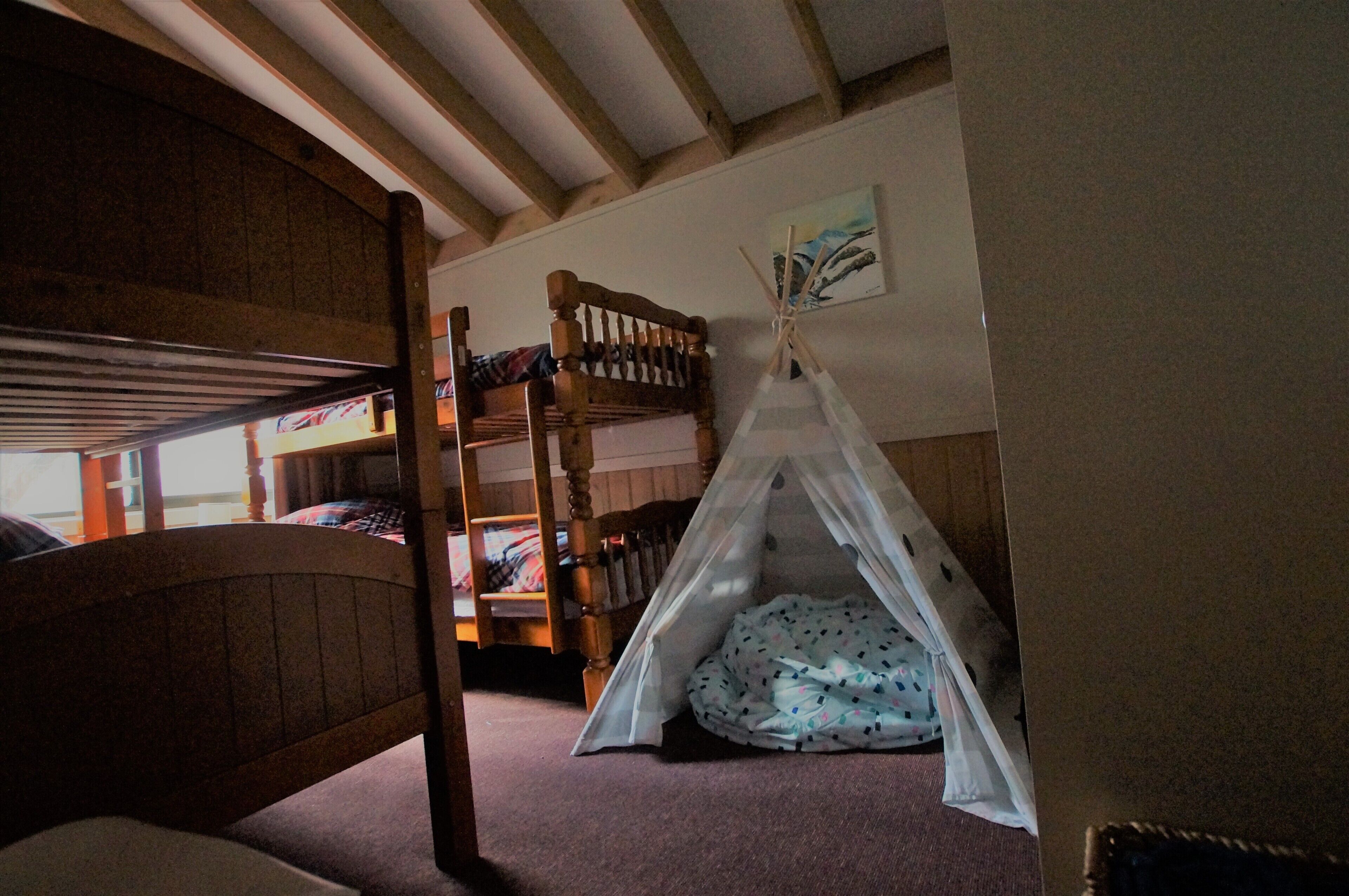 Habitación con literas, techo de madera, una estructura tipo tienda blanca y un cuadro en la pared.
