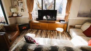A living room with a fireplace, a television, and a large window with curtains. - Mountain Retreat Suitable for 2 Families, Sleeps 8 (Mount Buller)