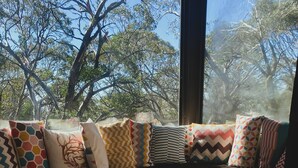 A room with a window seat adorned with various patterned cushions, a white furry rug, and a wooden stool. - Mountain Retreat Suitable for 2 Families, Sleeps 8 (Mount Buller)