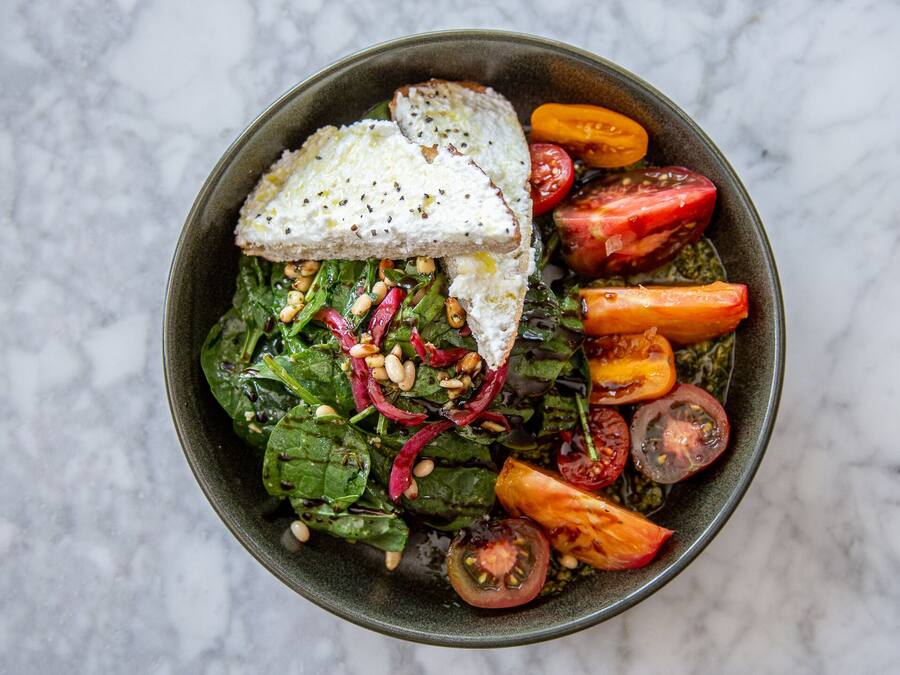 Un bol de salade contenant des tomates, des épinards et une tranche de pain.