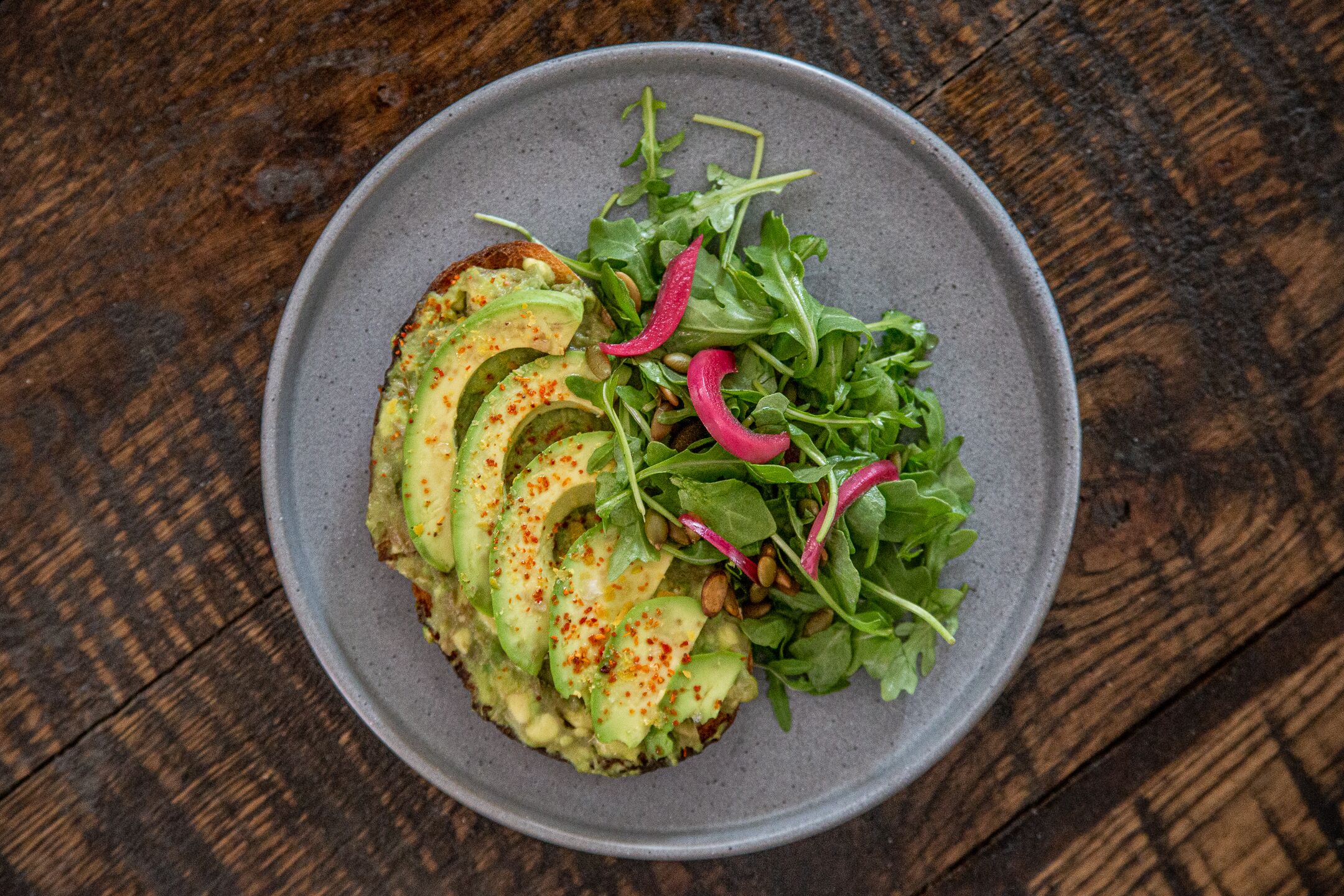 Ein Teller mit Essen, darunter Avocado-Scheiben, Grünzeug und Radieschen auf einem grauen Teller.