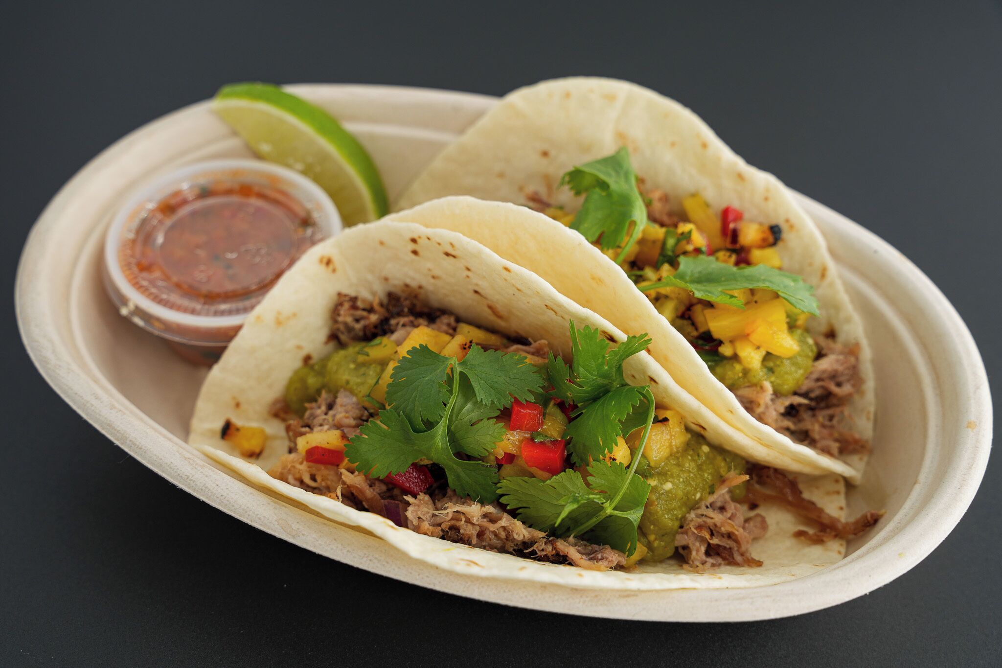 Tre tacos med forskellige fyld, en limeskive og en lille beholder med sauce.