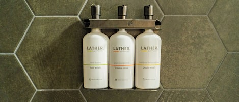 Três produtos Lather sobre uma estante metálica, com um painel de azulejos hexagonais ao fundo.