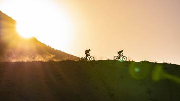 Two cyclists on a hill with a bright sun in the background.