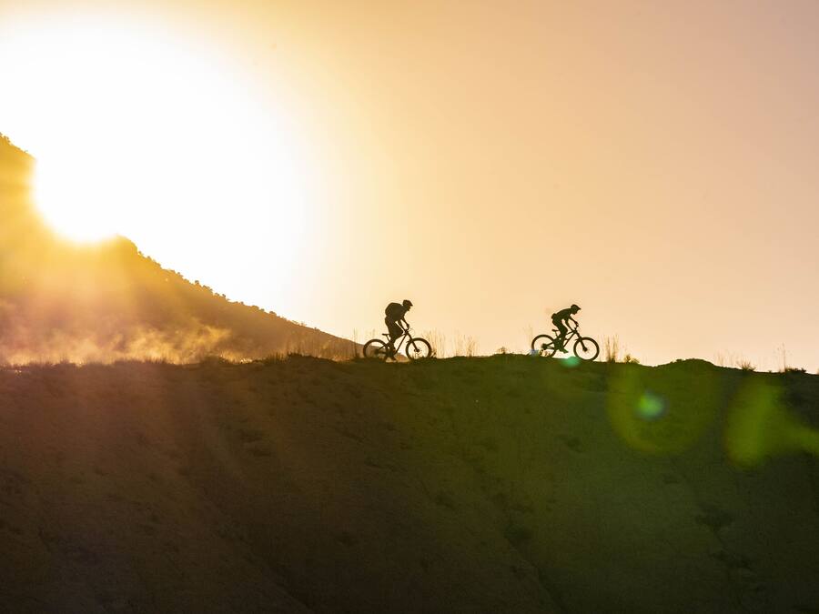 Two cyclists on a hill with a bright sun in the background.