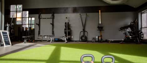 A gym with green flooring, kettlebells, and exercise equipment.