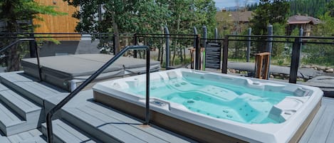 A hot tub on a wooden deck with steps leading up to it, surrounded by a metal fence and trees.