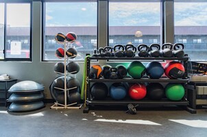 A gym with various exercise equipment, including kettlebells, medicine balls, and a rack of dumbbells.