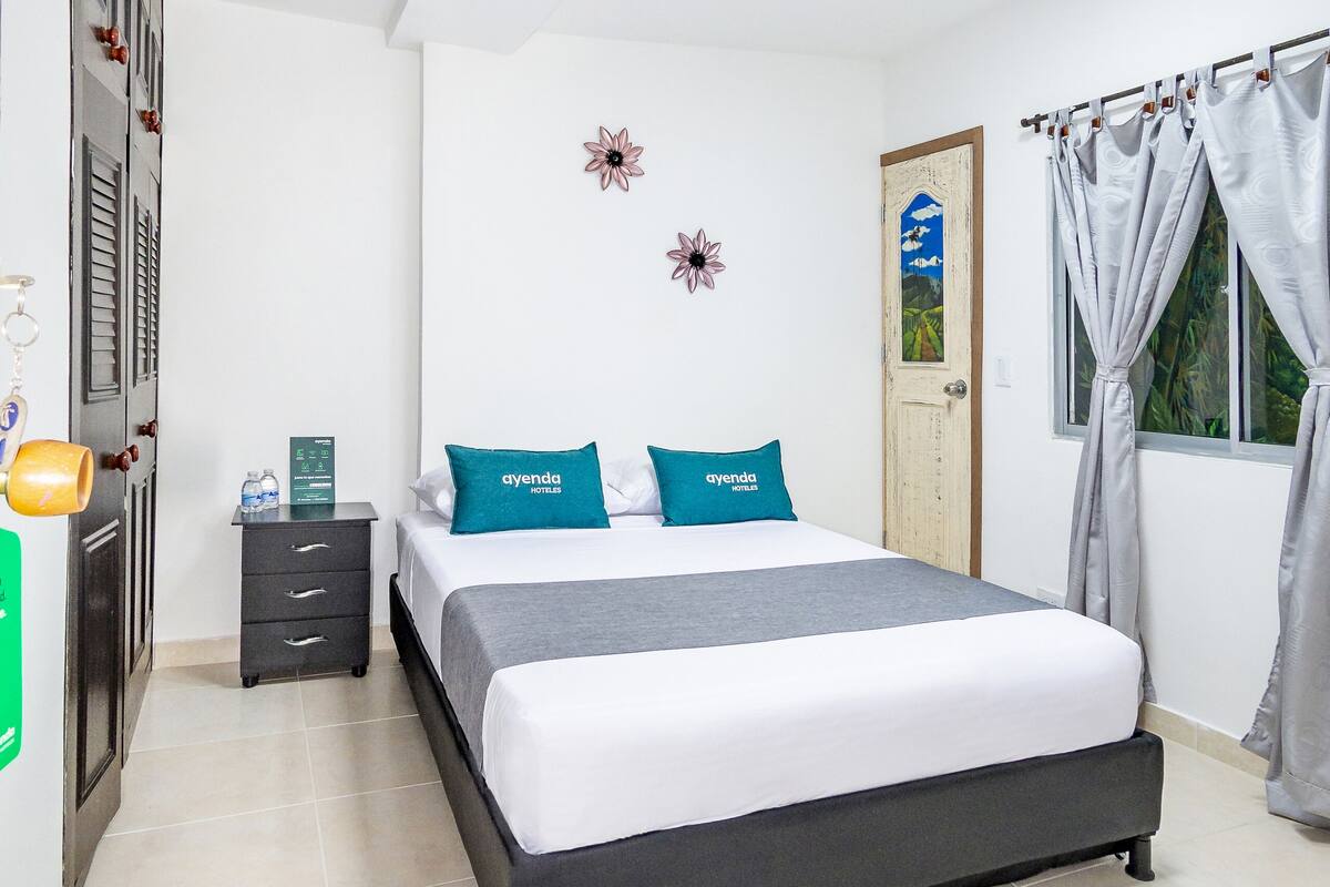 Una habitación de hotel con cama, mesita de noche, armario, puerta y ventana con cortinas.