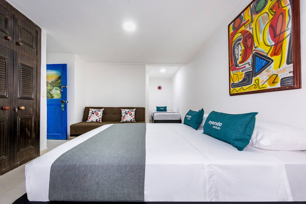 Habitación de hotel con una cama grande, una puerta azul y un cuadro abstracto colorido en la pared.