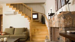 A living room with a wooden staircase, a stone fireplace, and a flat-screen TV mounted on the wall. - Beautiful 3-Bed  Sea Front Villa in Agios Nikolaos (Agios Nikolaos)