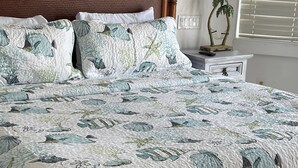 Una cama con colcha de estampado floral, cabecera de madera y mesita de noche con una lámpara y una planta.