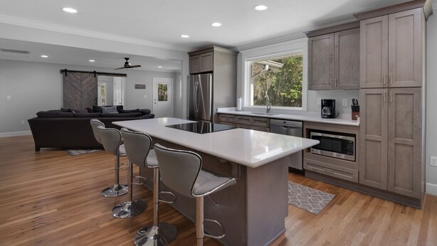 A modern kitchen with a central island, bar stools, stainless steel appliances, and wooden cabinets.