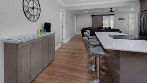 A modern kitchen with a bar area, wooden flooring, and a large wall clock.