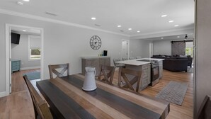 A modern kitchen with a dining area, featuring a wooden table, chairs, and a clock on the wall.