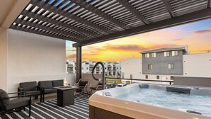 A rooftop terrace with a hot tub, outdoor seating, and a view of the sunset.
