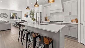 A modern kitchen with white cabinets, a central island with bar stools, pendant lighting, and a view of the outdoors.