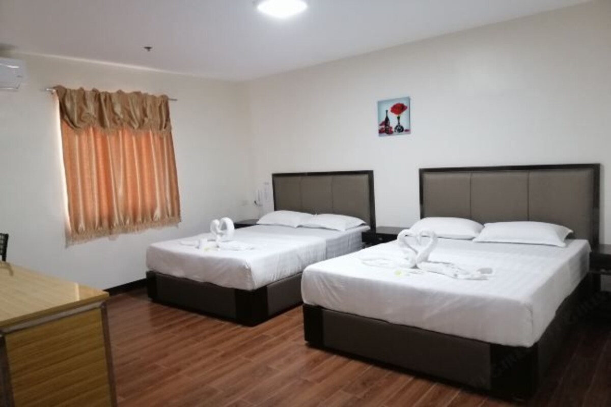 Habitación de hotel con dos camas individuales, un escritorio de madera y una ventana con cortinas.