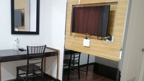 Una habitación con un escritorio de madera, dos sillas, un espejo y un televisor instalado en un panel de madera.