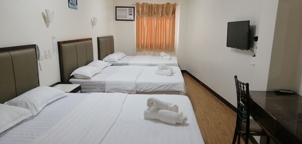 A hotel room with three single beds, a desk, a chair, a television, and a window with curtains.